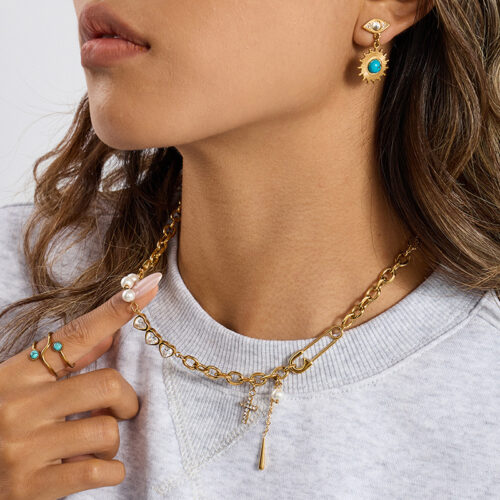 Gold safety pin necklace with pearl accents, heart cubic zirconia links, cross charm, star pendant, and chunky chain details